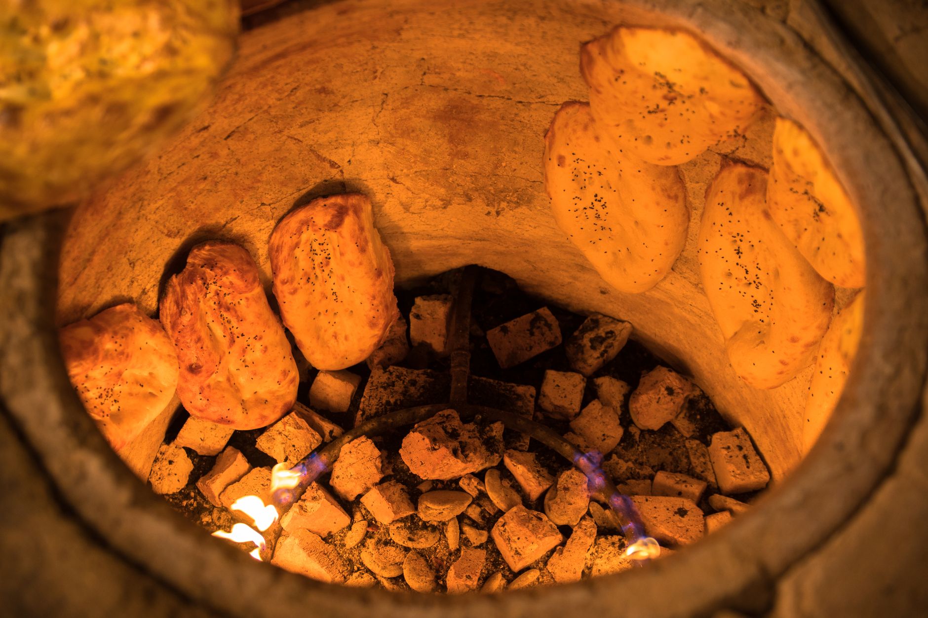 Flames and smoke rising from a tandoor oven as naan cooks inside, at night